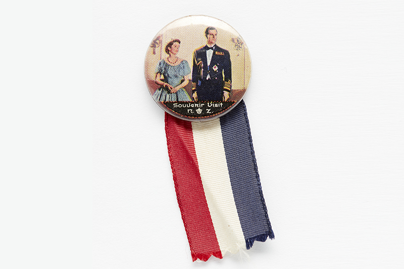 Metal badge with ribbon with a picture of Queen Elizabeth and Duke of Edinburgh on it with the text Souvenir visit 1953