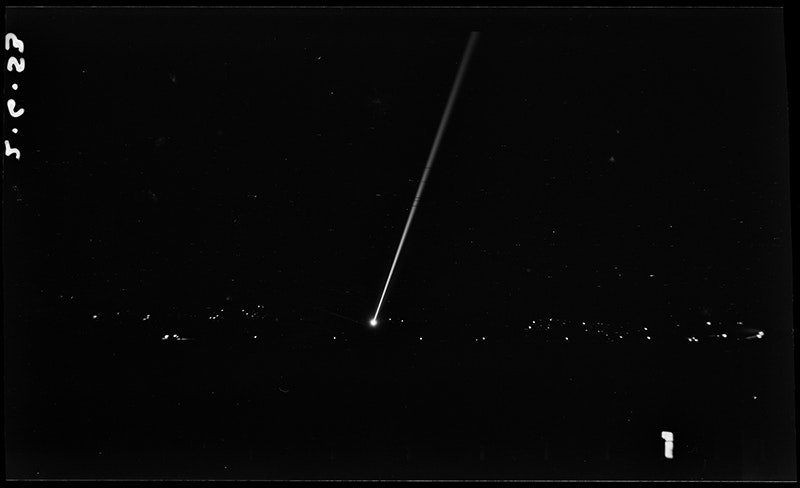 A largely black photo with a single long white beam of light and some other white dots indicating lights