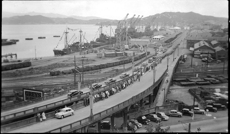 A sweeping photo with people lining the motorway and ships docked against the port
