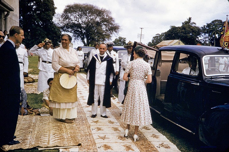 Duke of Edinburgh, Queen Sālote Tupou III and Queen Elizabeth II stand outside a car, standing on tapa, in preparation of getting into the car