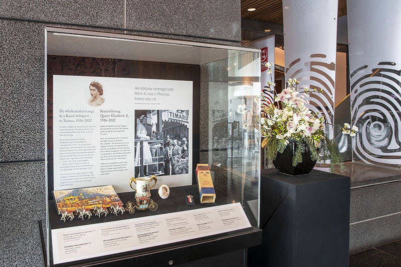 Photograph of a display case filled with objects, such as a periscope, a tankard, and a replica of the Queen’s coronation horse-drawn carriage