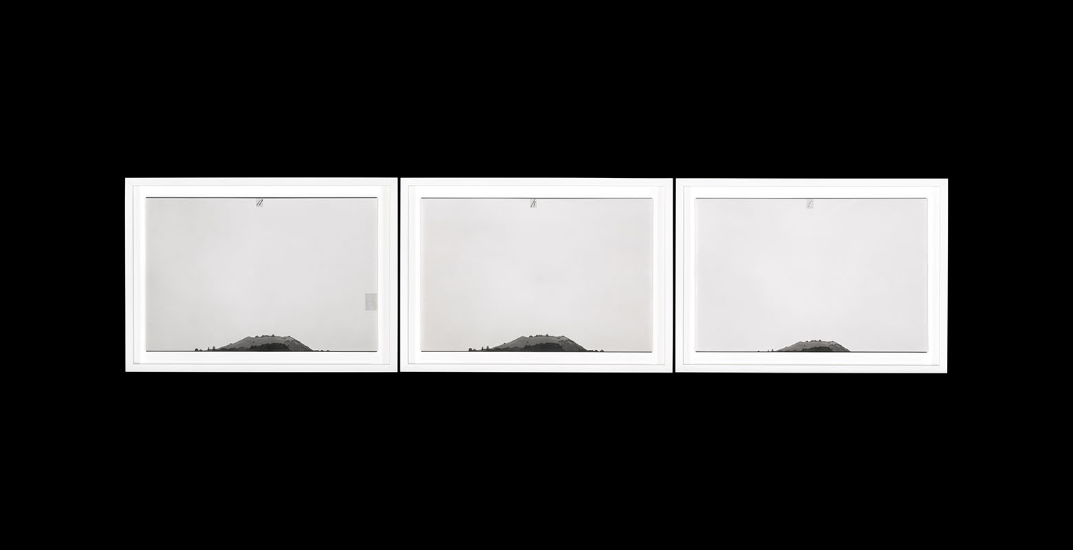A set of three photographs in identical white frames. All photos depict a hilltop, framed at the bottom to allow the cloudy sky to take up the vast majority of the photograph. In addition, a letter is written at the top of each photo: H, I, A.