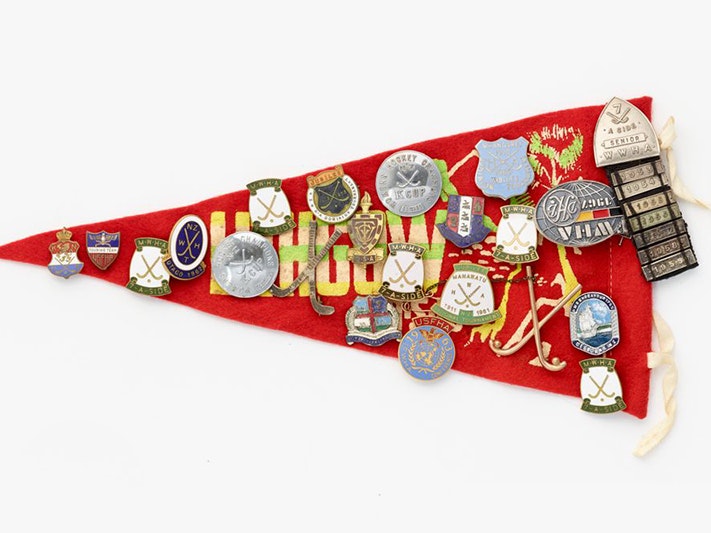 Souvenir pennant with badges, Unknown; manufacturer(s); 1950s–1960s. Gift of Enoka William John Stratton, in memory of Elva Marama Love (née Enoka), 2009. Te Papa (GH016352) A red felt triangle flag covered in metal and enamel badges for sport