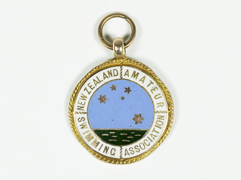Sports medal, New Zealand Amateur Swimming Association, about 1928, Birmingham, by Thomas Fattorini Ltd. Gift of Margaret L Bailey, in memory of Jean A. Dickson, 2006. CC BY-NC-ND 4.0. Te Papa (GH021311) A round badge with gold edging and an image of the sea with the Southern Cross in stars above it. It has the words New Zealand Amateur Swimming Association on it