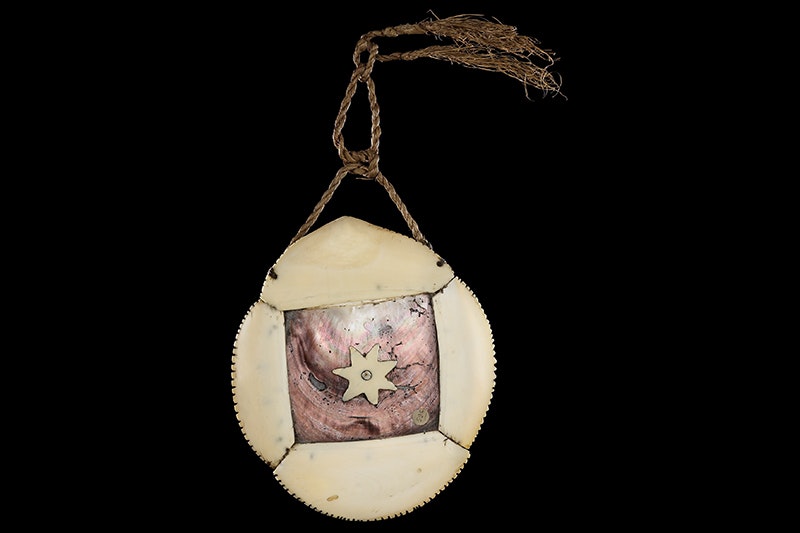 A breastplate made of bone and pearl hung on rope on a black background