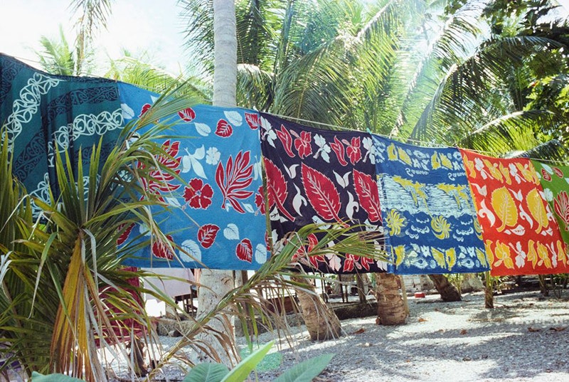 Several brightly coloured sheets are hanging on a washing line on beach with coconut  trees