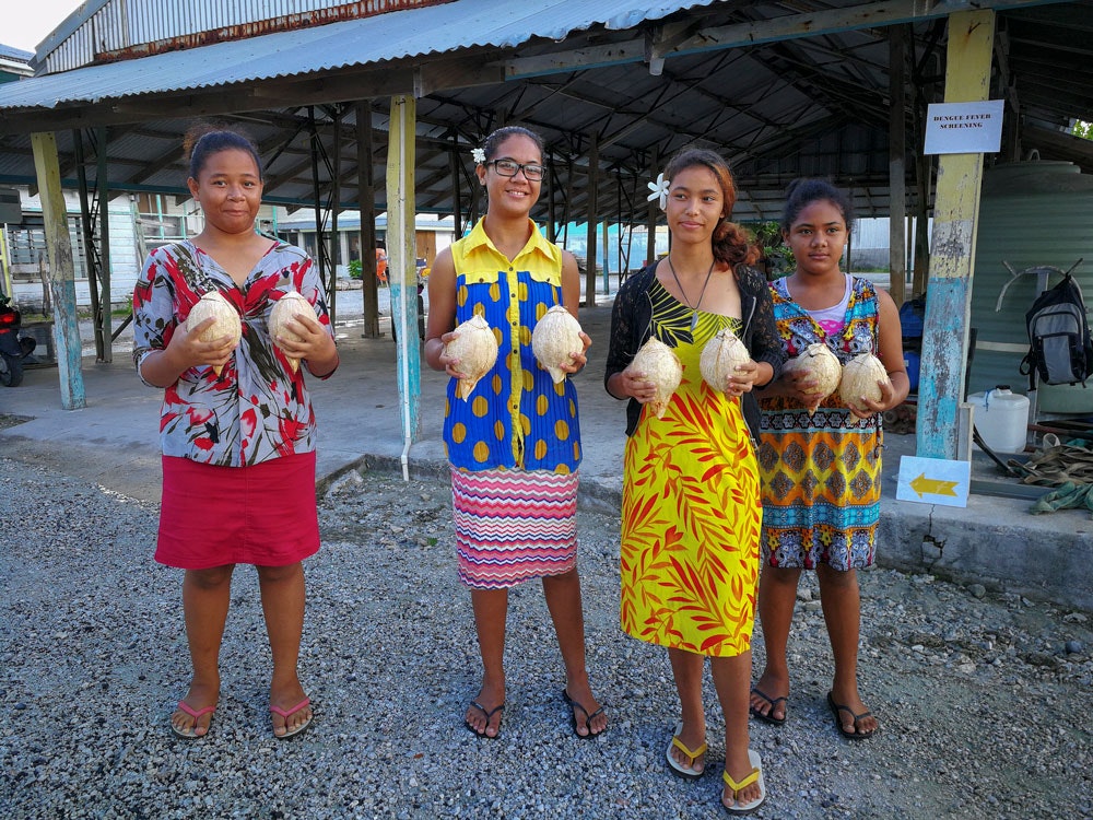 Four young girls are standing and all are holding a coconut in each hand