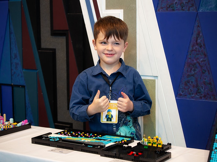 Autism NZ & LEGO Whānau Day 2021, 2021. Photo by Jo Moore. Te Papa (181743) A kid standing behind his lego creation holding two thumbs up
