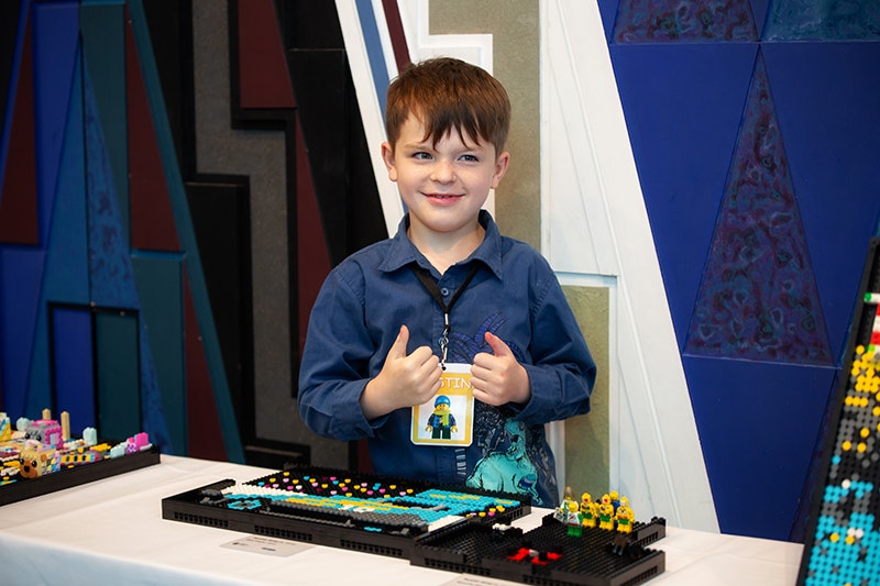 A kid standing behind his lego creation holding two thumbs up