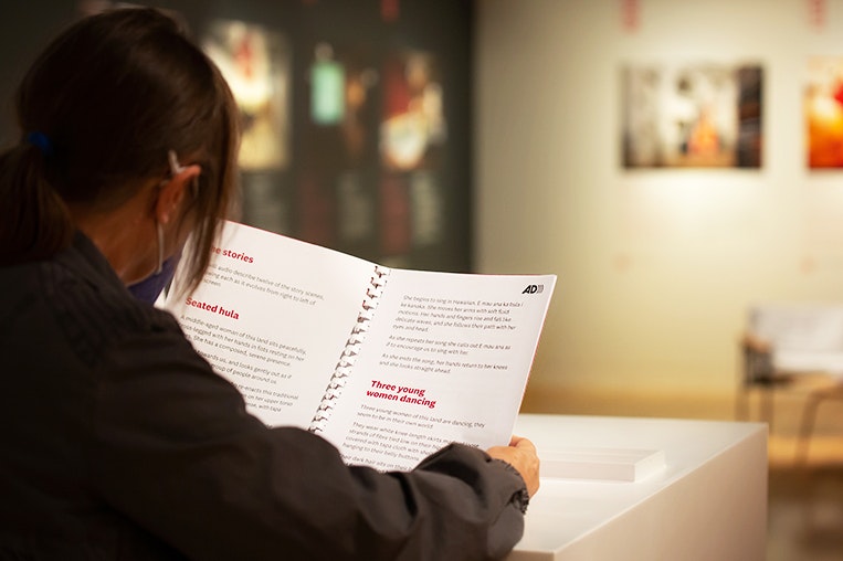 A woman reading a large-print booklet in a gallery setting