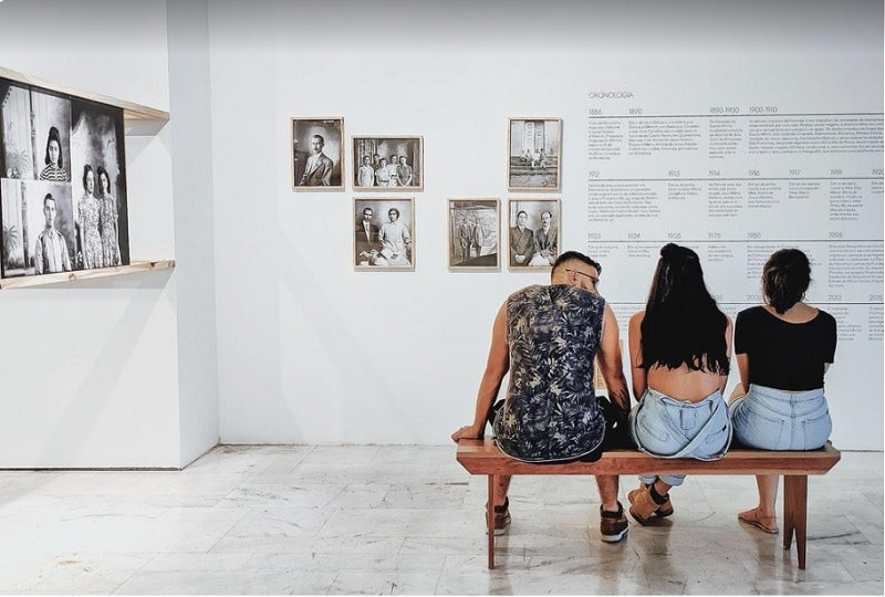 Three people sitting on a bench in an exhibition space