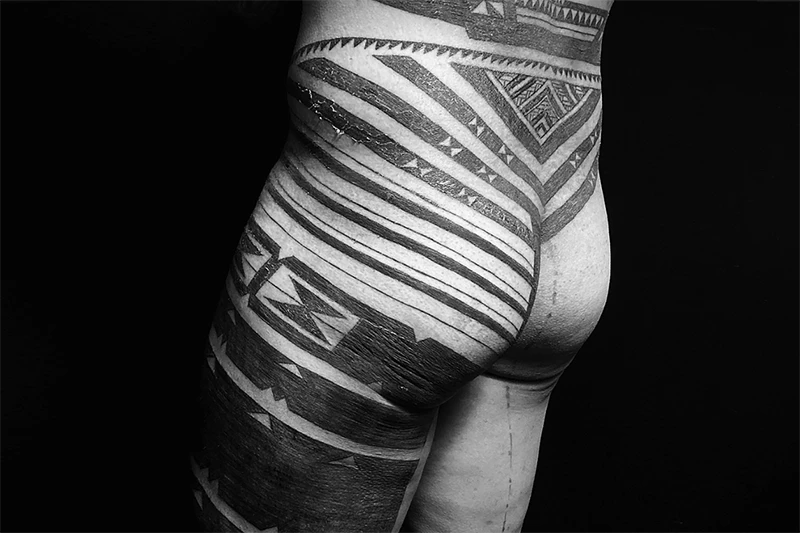 Black and white photo of the back and leg of a tattooed man