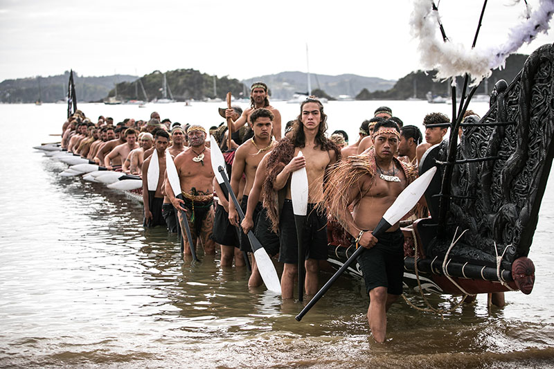 A group of Māori men lift a waka onto the shore