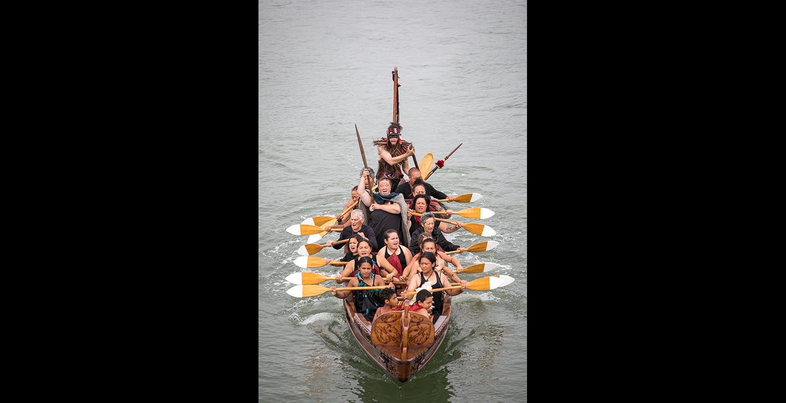 A group of men and women paddling a waka