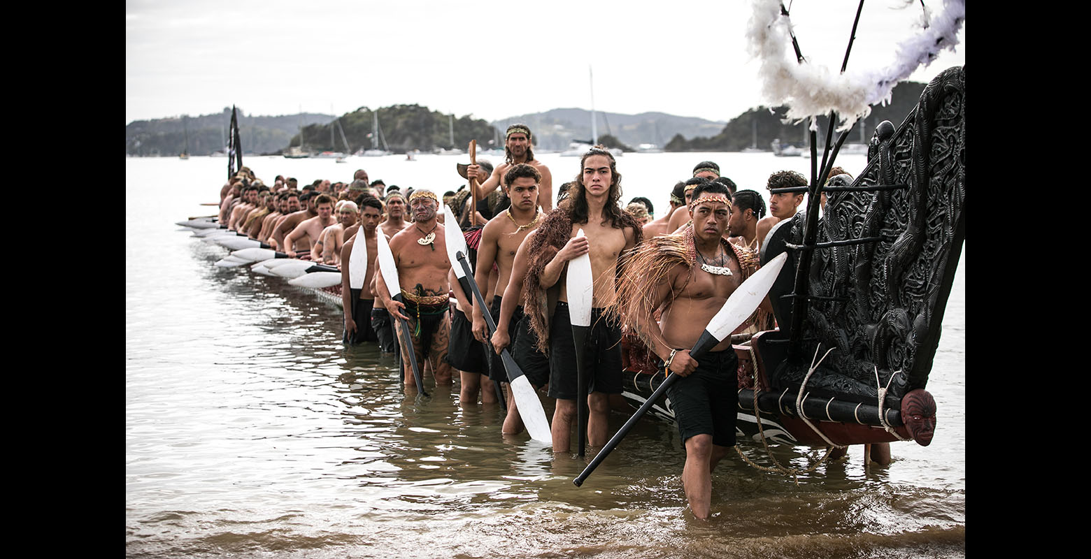 A group of Māori men lift a waka onto the shore
