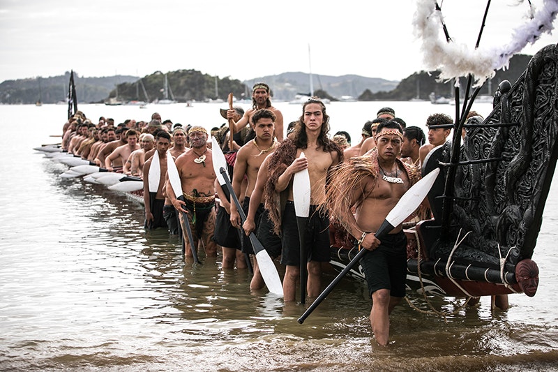 Many men sitting and standing on an carved canoe