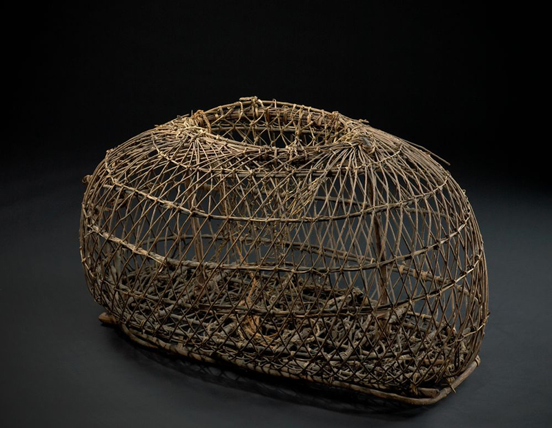 A woven wooden crayfish trap photographed with a black background.