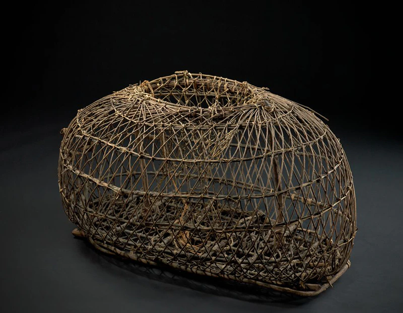 A woven wooden crayfish trap photographed with a black background.