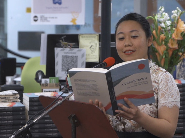 Still from Chinese Languages in Aotearoa: Mandarin, with poet Ya-Wen Ho, 2021, by Shijia Chen A woman stands in front of a microphone reading from a book in a book store