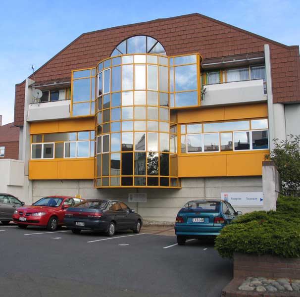 A white and yellow building with cars parked in front of it.