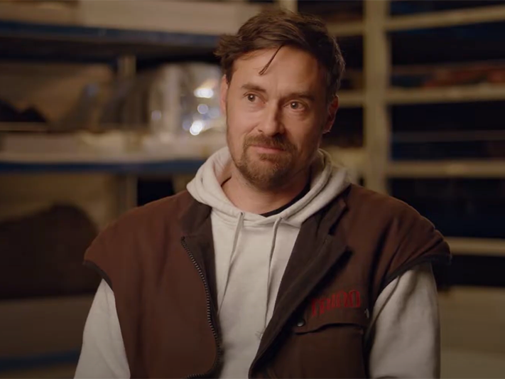 Matthew McIntyre Wilson. Te Papa A man with a beard is looking off camera at someone interviewing him. He is in a museum storeroom.