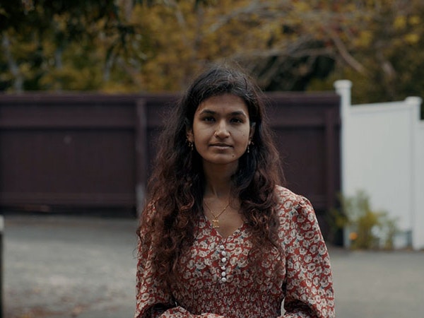Sehar Moughal, 2022. Photo by Julie Zhu A woman poses for a photo, standing in front of a brown fence