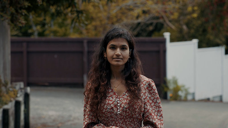 A woman poses for a photo, standing in front of a brown fence