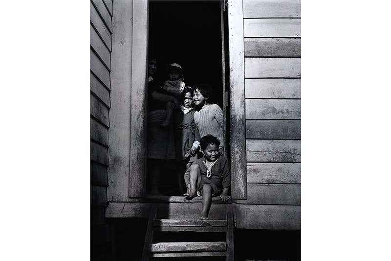 Cover image for Washday at the pa. A black and white photo of children sitting and standing on the doorstep of a house