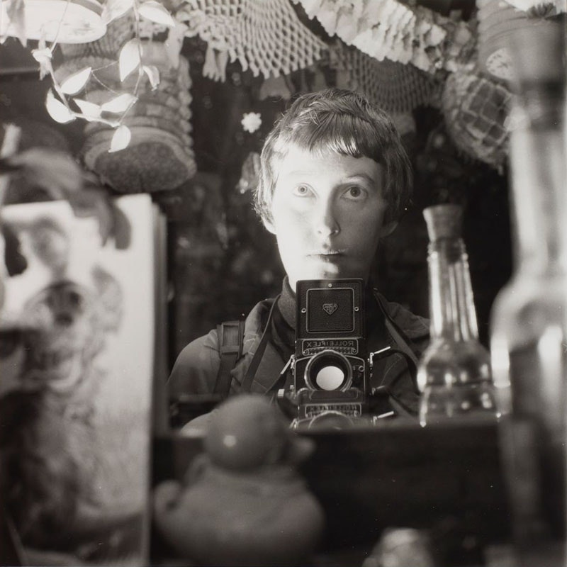 Black and white photo of a woman taking a photo of herself in the mirror with a Rolleiflex box camera