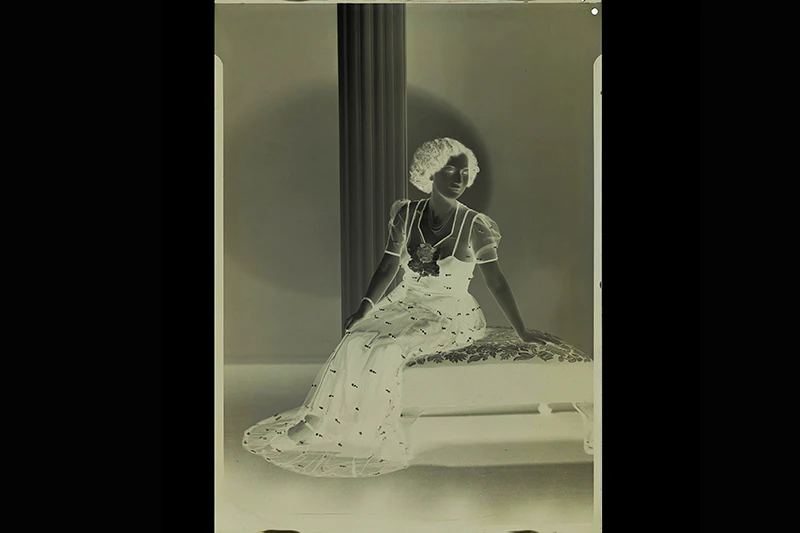 Negative of view of a photograph of a woman in a long dress sitting on a settee.