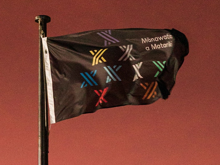 The Mānawatia a Matariki flag flies during the 2022 hautapu at Te Papa, 24 Jun 2022. Te Papa A black flag with the logo of the Matariki public holiday, consisting of nine stylised stars, flies in the early morning Wellington breeze, with an orange sunrise behind it