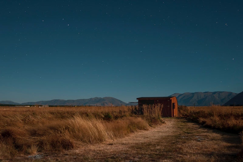Photo of a country hut in the foreground and a star-filled night sky behind it