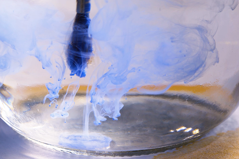 A paintbrush in a glass of water and swirling blue paint