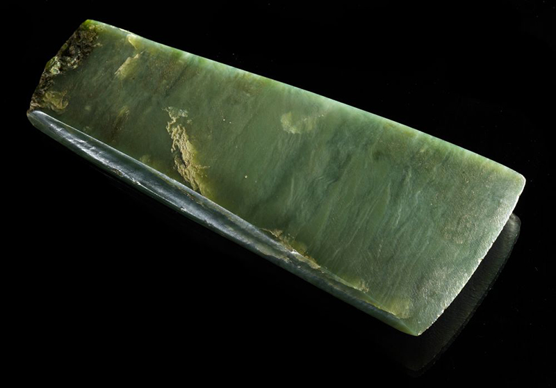 An adze made from pounamu greenstone on a black background.