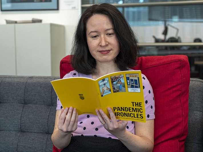 Grace Gassin, Curator Asian New Zealand Histories, 2022. Photo by Daniel Crichton-Rouse. Te Papa Grace sits on a couch with a large red cushion reading a copy of The Pandemic Chronicles