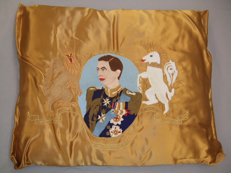 Embroidered cushion, King George VI, 1937, Dunedin, by Miss Nancy Robertson. Gift of The Merrick Girls, 2012. CC BY-NC-ND 4.0. Te Papa (GH017530) A gold satin cushion with an image of a king and a unicorn embroidered on it.
