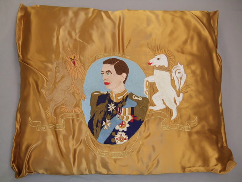A gold satin cushion with an image of a king and a unicorn embroidered on it.
