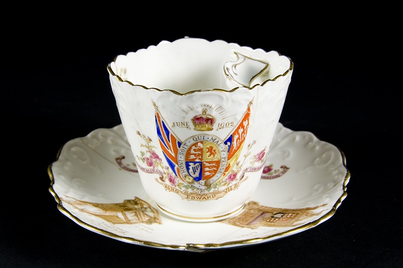 A cup and saucer with royal markings and images on it.