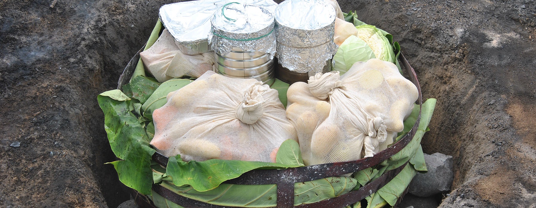 Food wrapped up, in a pit, ready to be covered and cooked in a hāngi