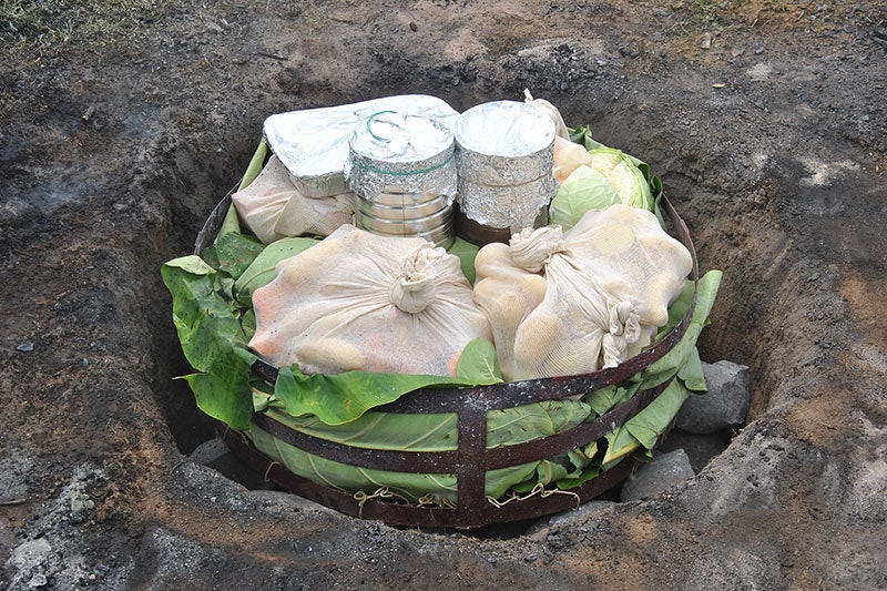 Food wrapped up, in a pit, ready to be covered and cooked in a hāngi