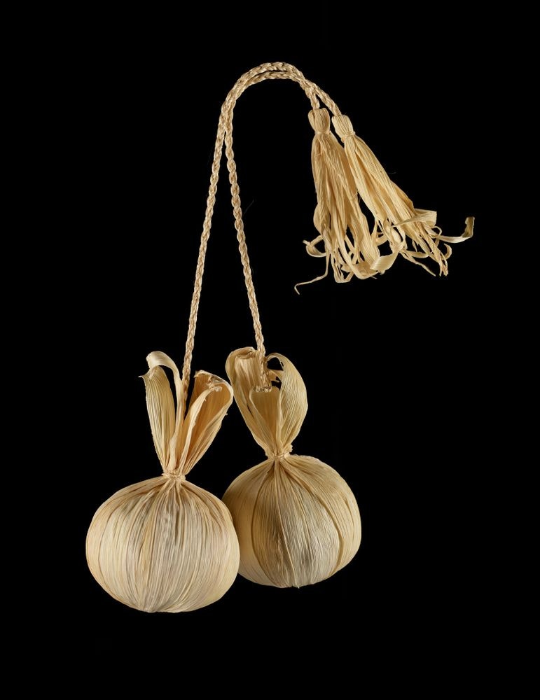 Two round balls made of dried flax with plaited flax connected to each of them.