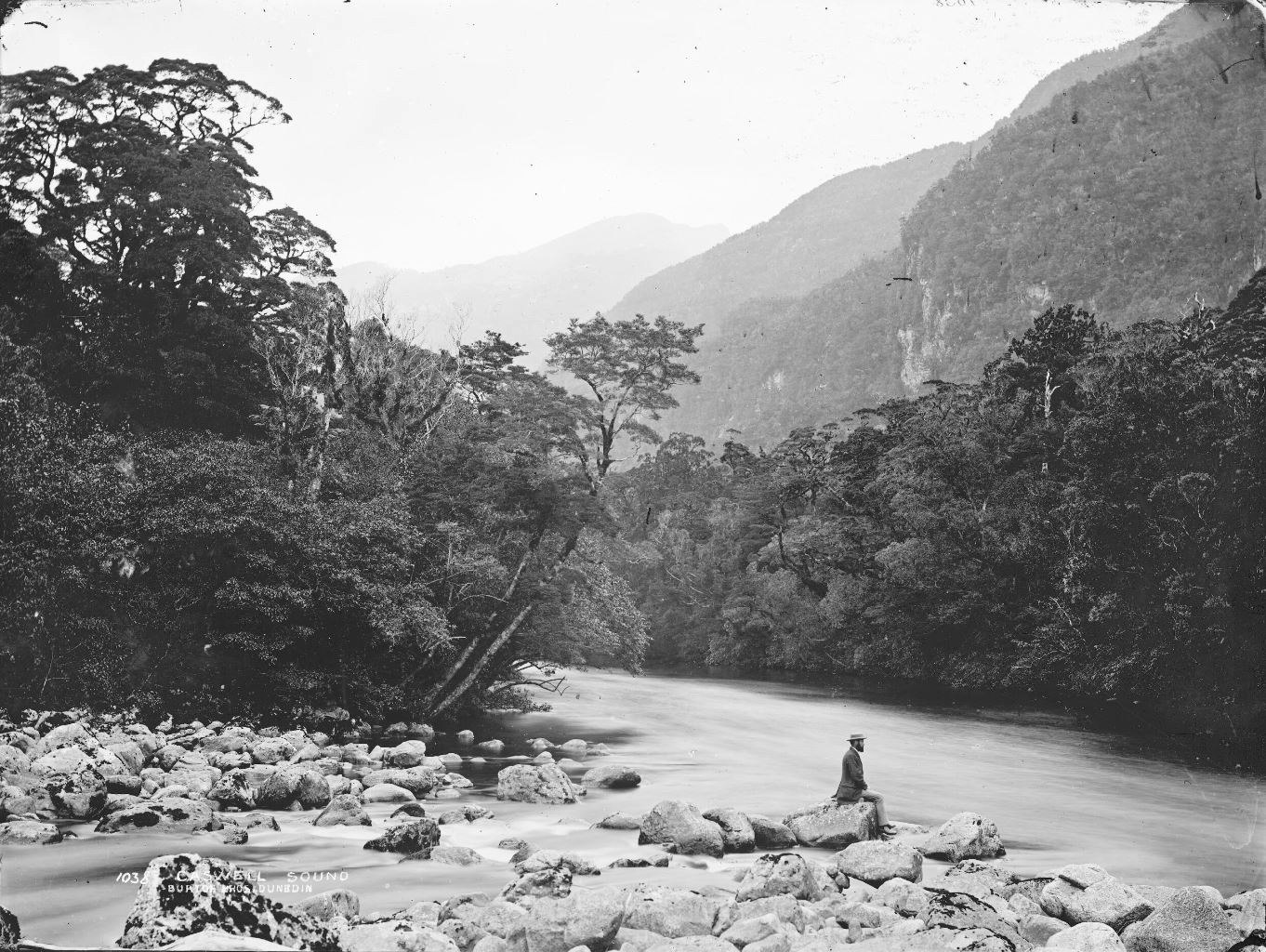 A man sits on a rock by the river