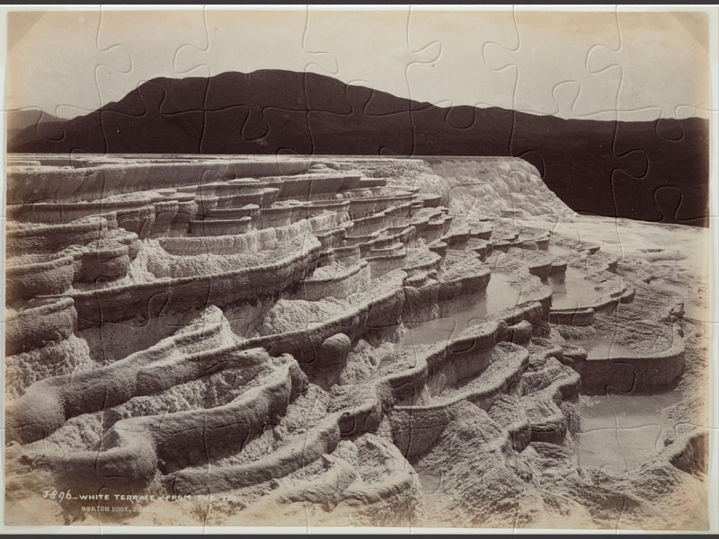 Black and white photo of silica geothermal pools in a terrace formation with dark mountains in background