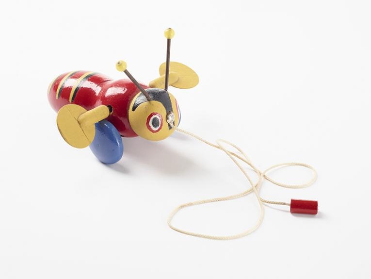 A wooden toy on a string, it is a brightly coloured bee with wings that make clacking sounds as it is pulled along.