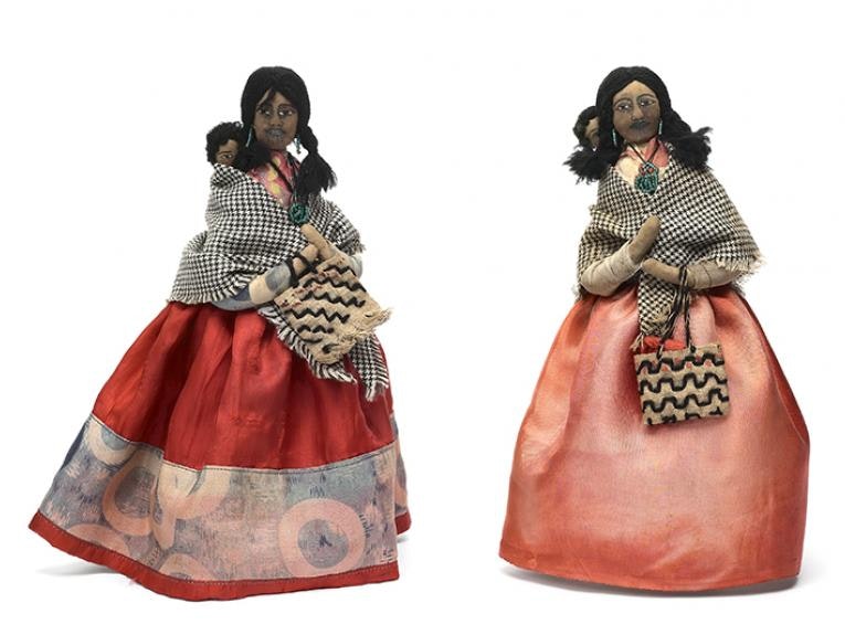 A doll made from soft materials of a Māori with a baby on her back wrapped in a blanket.