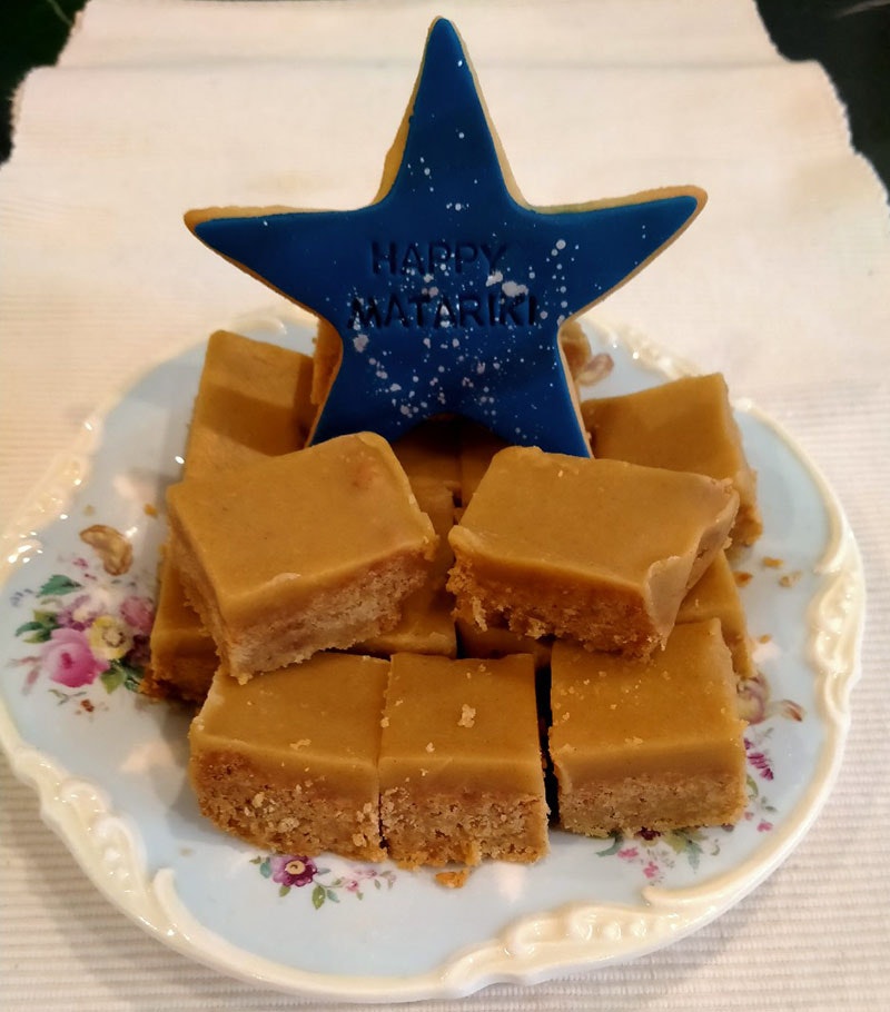 A plate of ginger crunch, with a biscuit in the shape of a star, coated in blue icing with the words "Happy Matariki" on it