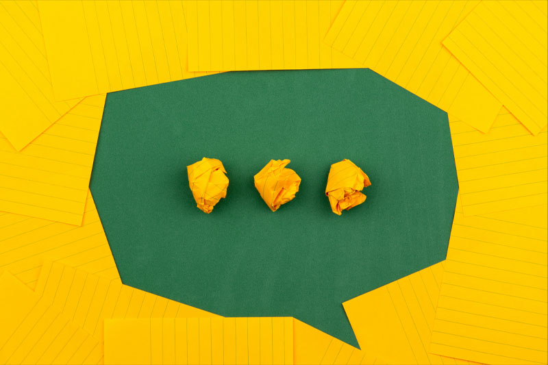 Three crumpled yellow papers on green surface surrounded by yellow lined papers suggesting a thinking bubble