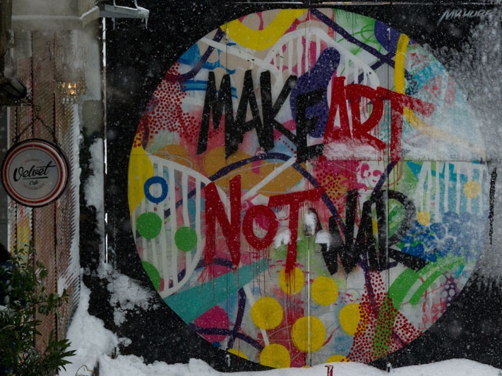 Randy Tarampi, ‘Make Art Not War’ mural, Istanbul, Turkey, 2017. Unsplash Photo of a wall with graffiti on it. The graffiti is a colourful circle and inside it is written "Make Art Not War". It has been snowing and snow has settled on the ground at the wall
