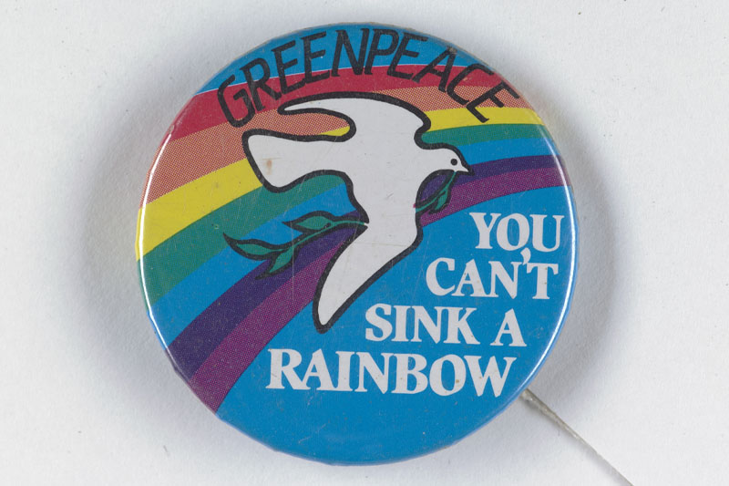 Blue-coloured badge with a rainbow and white dove on it. Text reads “Greenpeace” and “You can’t sink a rainbow”