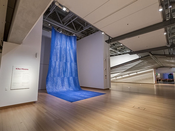 Mataaho Collective, Kiko Moana, 2016, polyethene tarpaulin and cotton thread. Te Papa (ME024286) ‘Kiko Moana’ on display in Te Papa. A large sheet of blue tarpaulin hangs from the ceiling, and drapes onto the floor, resembling a waterfall